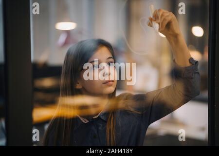 Girl drawing on glass pane in office Stock Photo