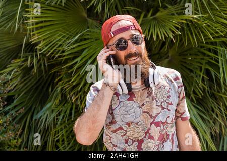 Mature man with red basecap, sunglasses and white headphones using smartphone Stock Photo