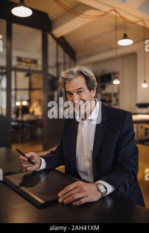 Portrait of smiling senior businessman using graphics tablet at desk in office Stock Photo