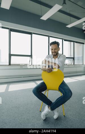 Portrait of confident mature businessman sitting on yellow chair in empty office Stock Photo