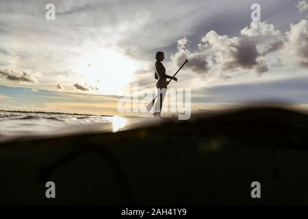Female SUP surfer at sunset, Bali, Indonesia Stock Photo