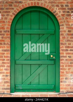 Closed green painted wooden door in arch opening in red brick wall, Barnsdale Gardens, Rutland, England, UK Stock Photo