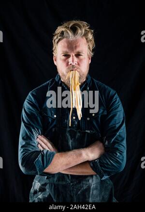 Hobby chef holding fresh tagliatelle pasta in his mouth Stock Photo