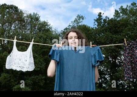 Portrait of young woman standing behind dress drying on clothesline Stock Photo