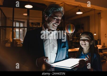 Happy senior buisinessman and girl with hot-air balloon and shining tablet in office Stock Photo