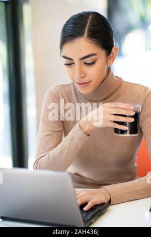 Young woman having a drink and using laptop in a cafe Stock Photo