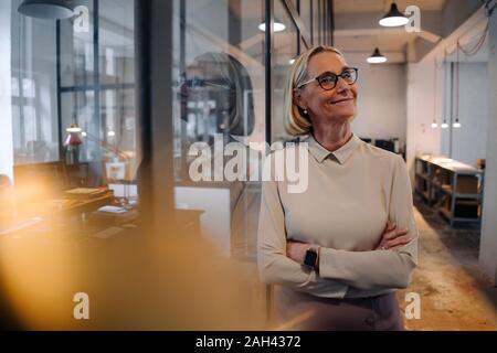 Portrait of smiling mature businesswoman leaning against glass pane in office