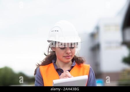 Female worker with clipboard taking notes on industrial site Stock Photo