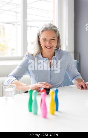 Laughing mature businesswoman playing with pins on desk in office Stock Photo