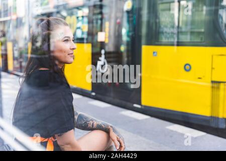 Portrait of tattooed young woman waiting at tram stop, Berlin, Germany Stock Photo