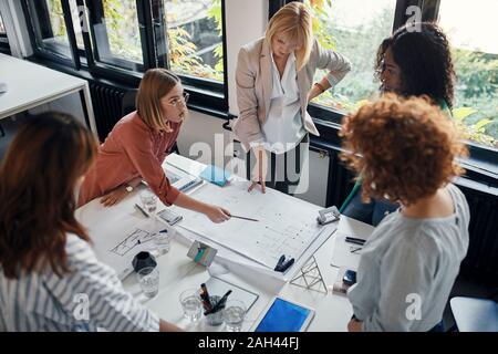 Businesswomen having a meeting in office with blueprints on table Stock Photo