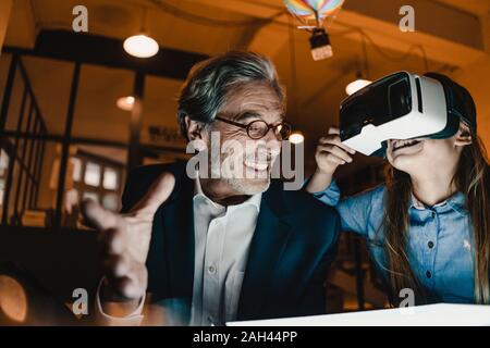 Happy senior buisinessman and girl wearing VR glasses with hot-air balloon in office