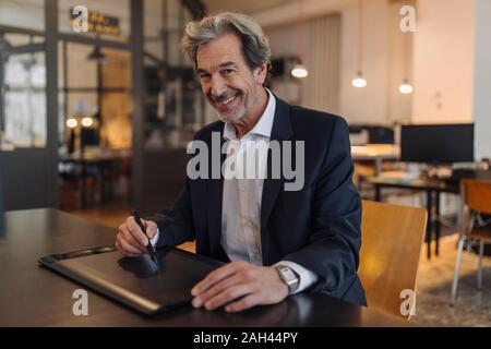 Portrait of smiling senior businessman using graphics tablet at desk in office Stock Photo