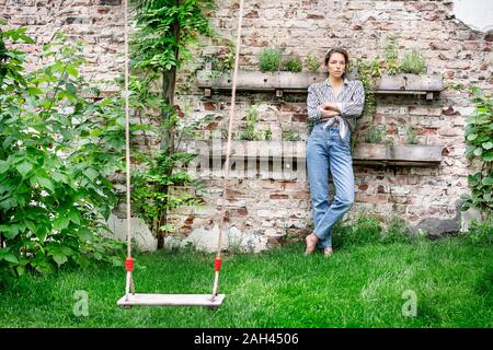 Young woman with arms crossed leaning on wall, looking sceptical Stock Photo
