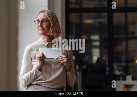 Mature businesswoman holding tablet at the window in office Stock Photo