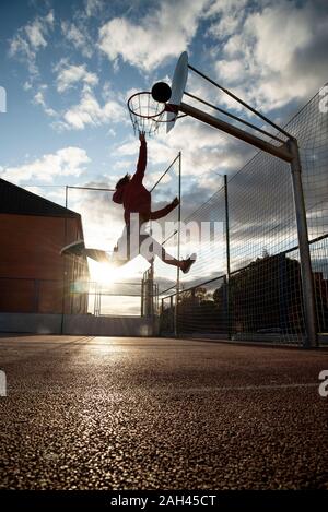 Teenager playing basketball, dunking against the sun Stock Photo