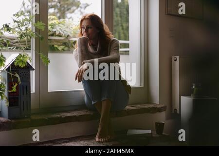 Mature woman sitting on steps of balcony door, daydreaming Stock Photo