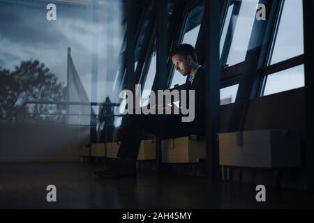 Businessman at the window in office working late using laptop Stock Photo