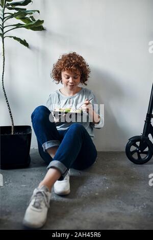 Businesswoman sitting on the floor in office having lunch break Stock Photo