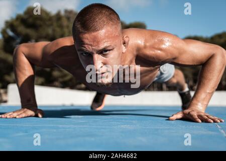 Portrait of barechested muscular man doing pushups outdoors Stock Photo