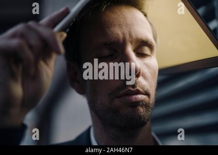 Businessman with closed eyes holding illuminated laptop above his head Stock Photo