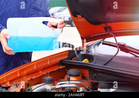 Driver with blue washer fluid in his hands, close up. Car maintenance concept. Filling windshield washer fluid on orange car. Stock Photo