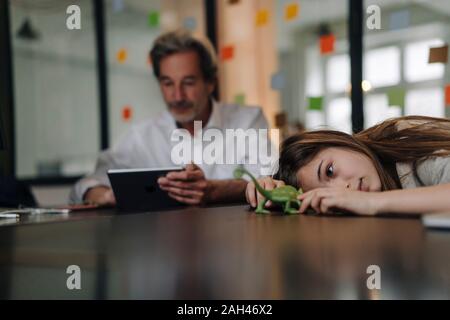 Senior buisinessman using tablet and girl playing with chameleon figurine in office Stock Photo