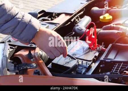 Measurement of battery voltage in a car. Car mechanic is using a multimeter with voltage range measurement. Stock Photo
