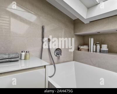 detail of the bathtub in foreground the faucet and some books in the niche in a modern bathroom in the attic Stock Photo