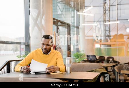 Man with reusable cup reading documents in a cafe Stock Photo