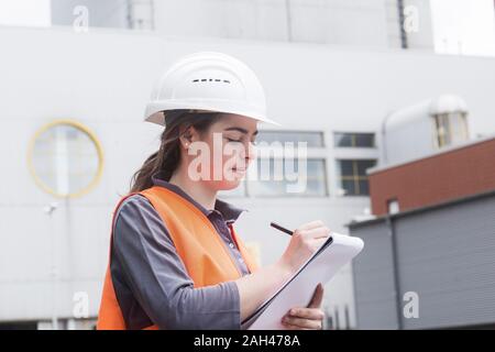 Female worker with clipboard taking notes at power plant Stock Photo