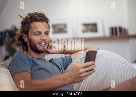 Smiling young man relaxing in beanbag at home using cell phone Stock Photo