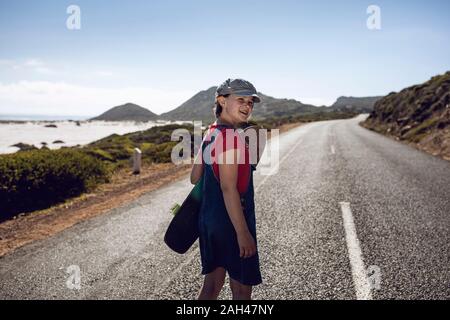 Portrait of smiling girl with skateboard standing on country road, Cape Town, Western Cape, South Africa Stock Photo