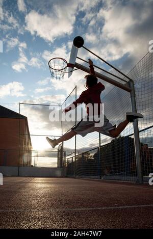 Teenager playing basketball, dunking against the sun Stock Photo
