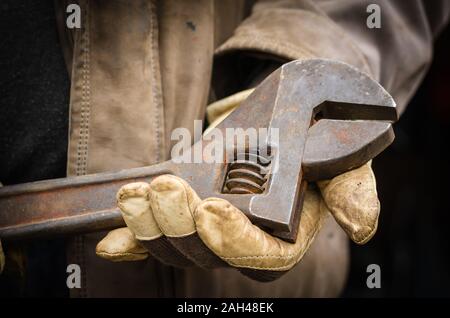 Rusty adjustable wrench in male hands. Mechanic in protective work gloves holds a huge wrench. Close-up. Eye level shooting. Stock Photo