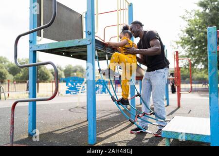 Father helping daughter on a rope ladder on a playground Stock Photo