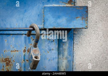 Close-up of an old metal door with anti-vandal protection against thieves. An open padlock is hanging on the door handle. Eye level shooting. Stock Photo