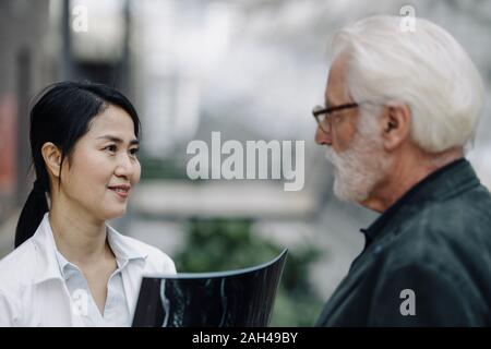 Smiling female doctor with x-ray and senior man talking Stock Photo