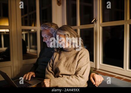 Senior couple using laptop on couch at home at night Stock Photo