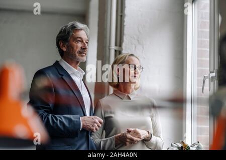 Confident businessman and businesswoman looking out of window in office Stock Photo