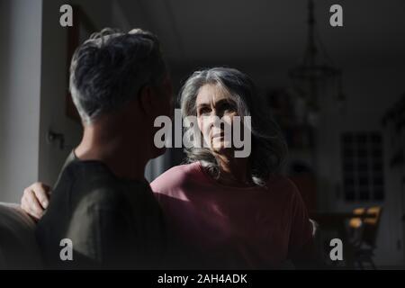 Serious senior couple sitting on couch at home in shadow Stock Photo