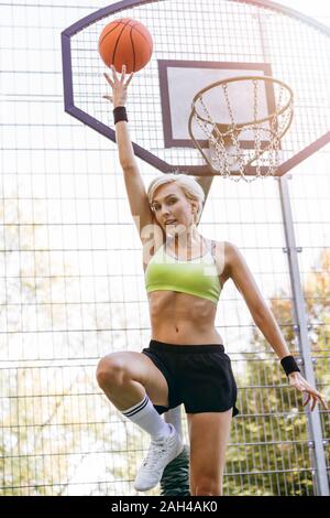 Blonde woman playing basketball, dunking Stock Photo