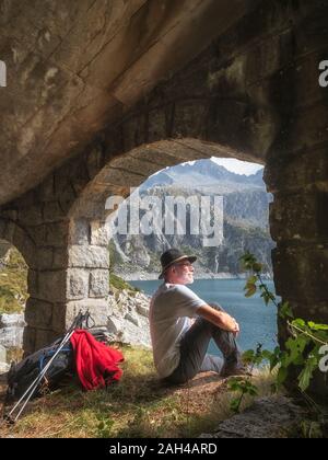 Italy, Hiker sitting under bridge, looking to Lago di Salarno Stock Photo