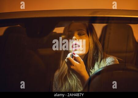 Portrait of blond woman in car applying lipstick Stock Photo