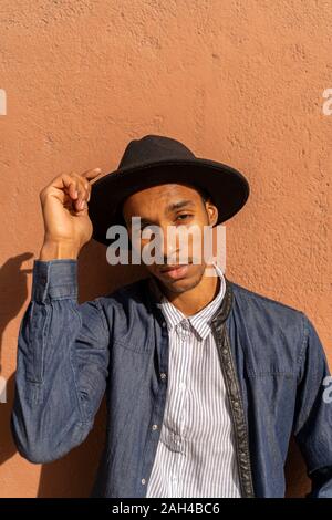 Portrait of stylish young man wearing a hat at a wall Stock Photo