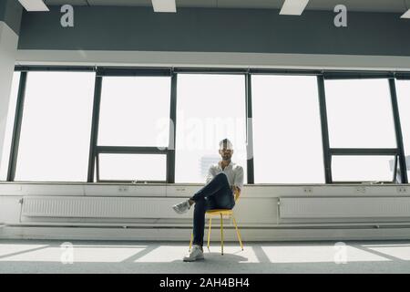 Mature businessman sitting on yellow chair in empty office Stock Photo
