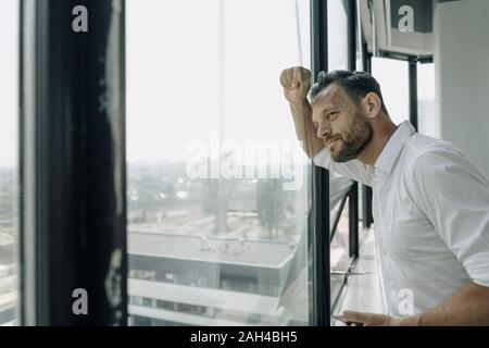 Mature businessman looking out of window in office Stock Photo