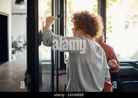 Colleagues writing on sticky notes at glass pane in office Stock Photo