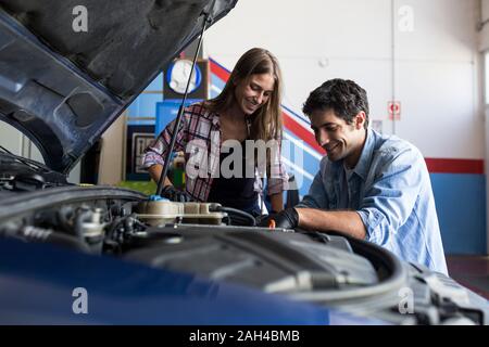 Cheerful man and young woman working together on car repair service and fixing car engine Stock Photo