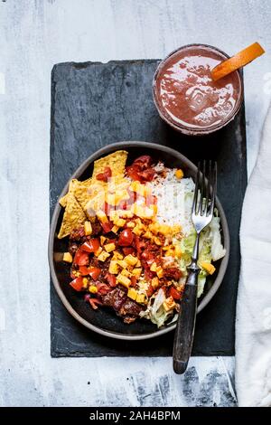 Bowl of nachos with, chili con carne, rice, lettuce, cheese, tomatoes and glass of refreshing paloma cocktail Stock Photo